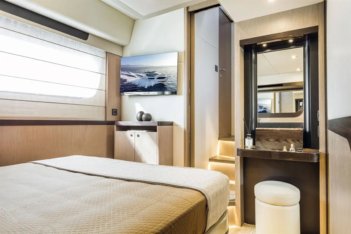 Modern yacht cabin featuring a double bed, TV, storage, and a stylish dressing table with a mirror. Natural light illuminates the space.